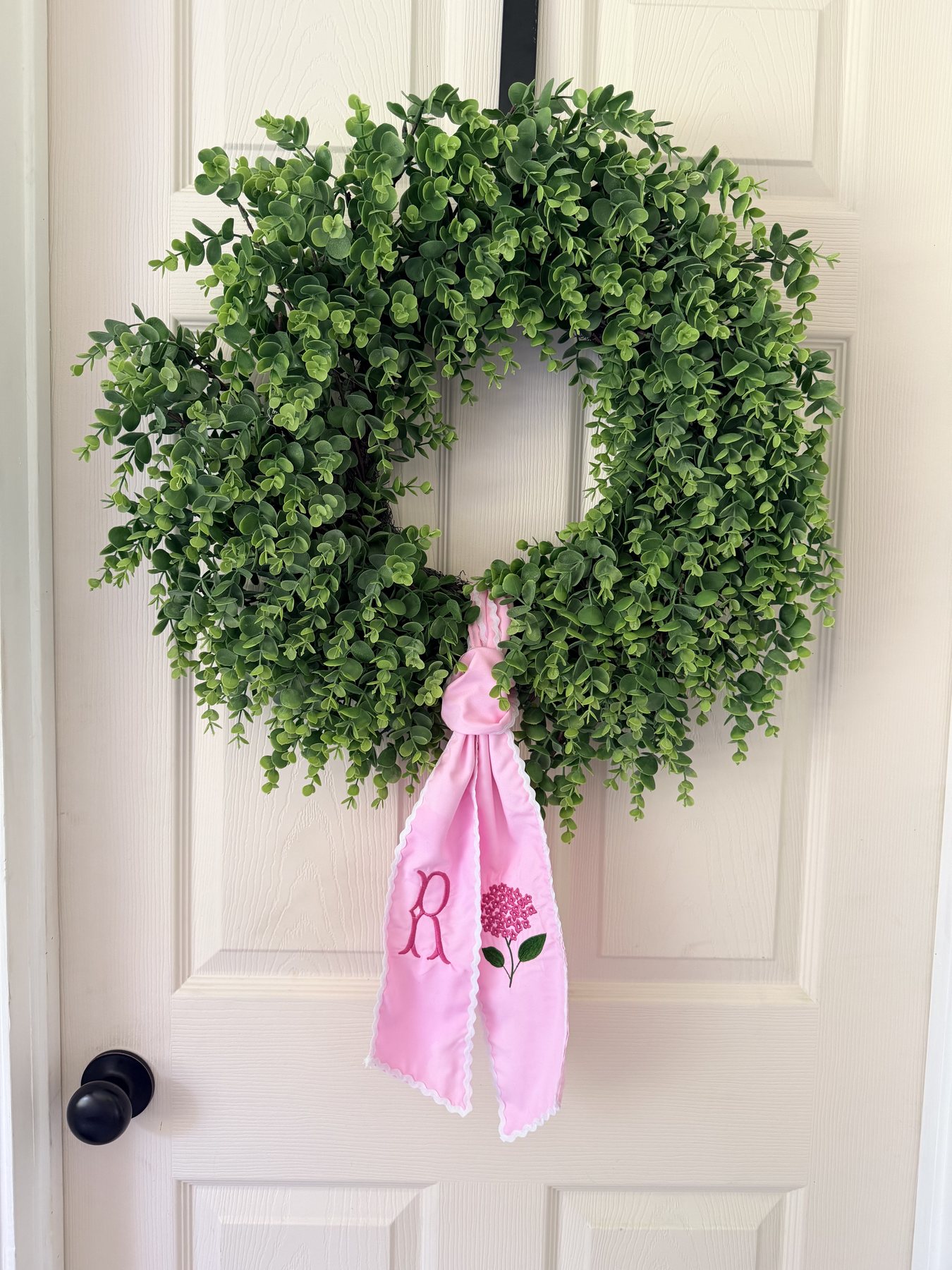 Green wreath with a pink and white bordered embroidered sash